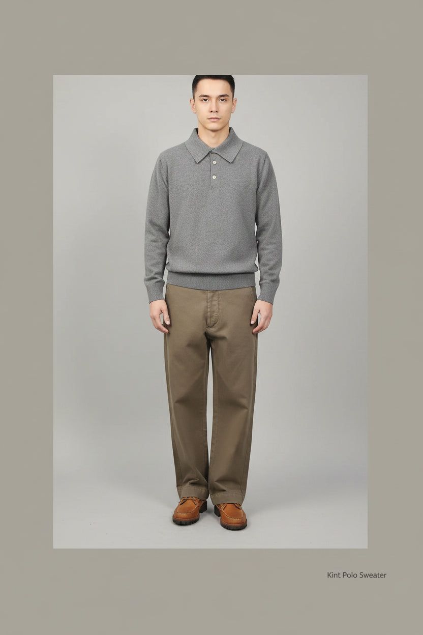 Person wearing a gray sweater and brown pants standing against a green background with a decorative chair.