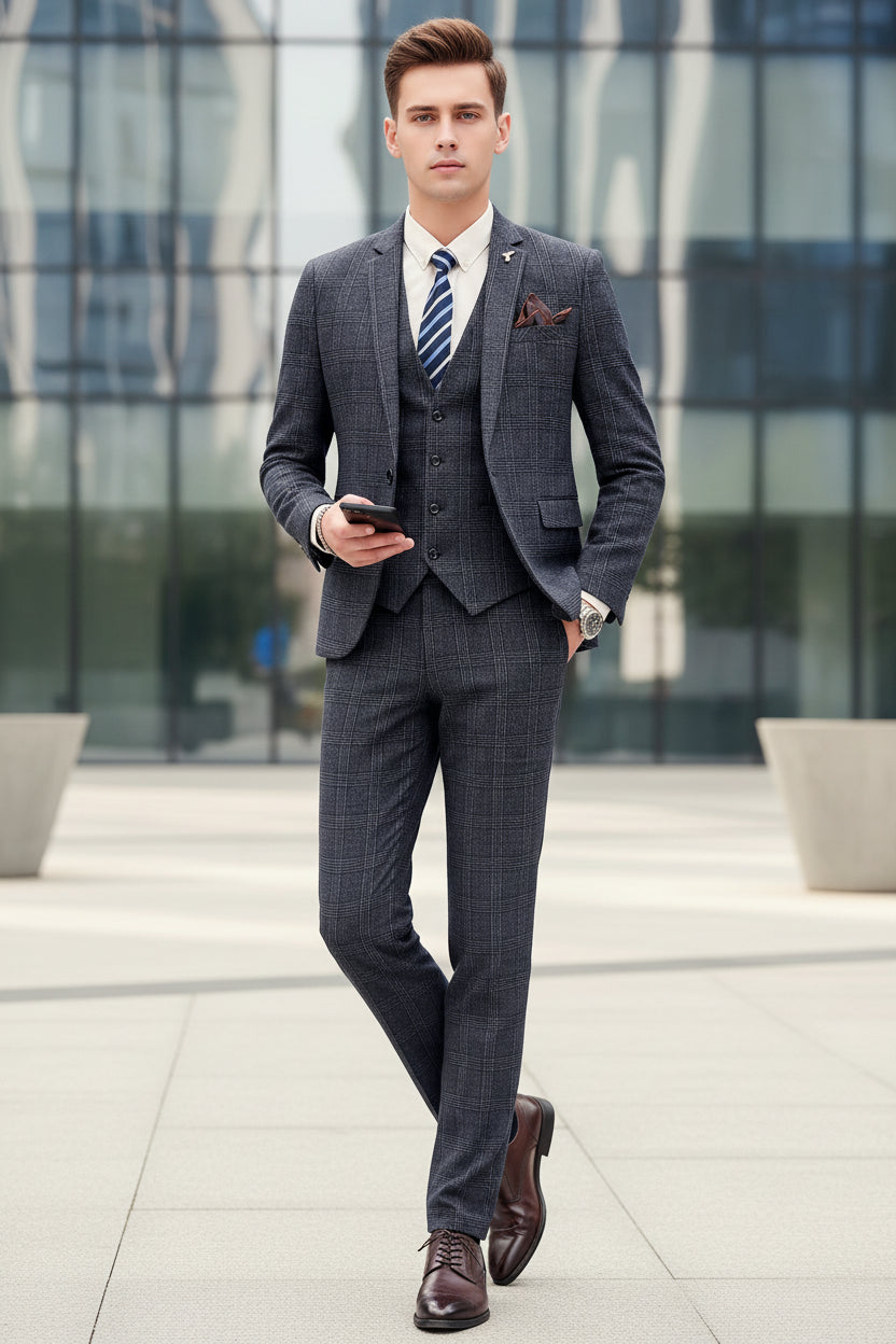 Man in a gray checkered suit holding a phone against a marble wall.
