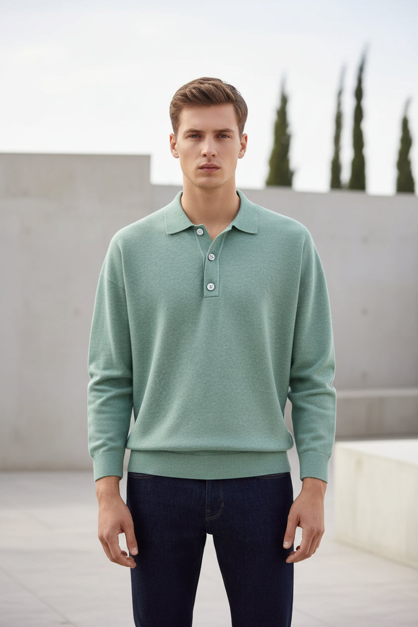 Person wearing a light green sweater over a collared shirt with dark jeans on a plain background
