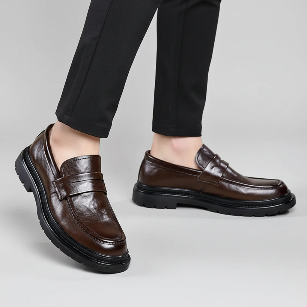 Brown leather loafers worn with black pants on a beige background