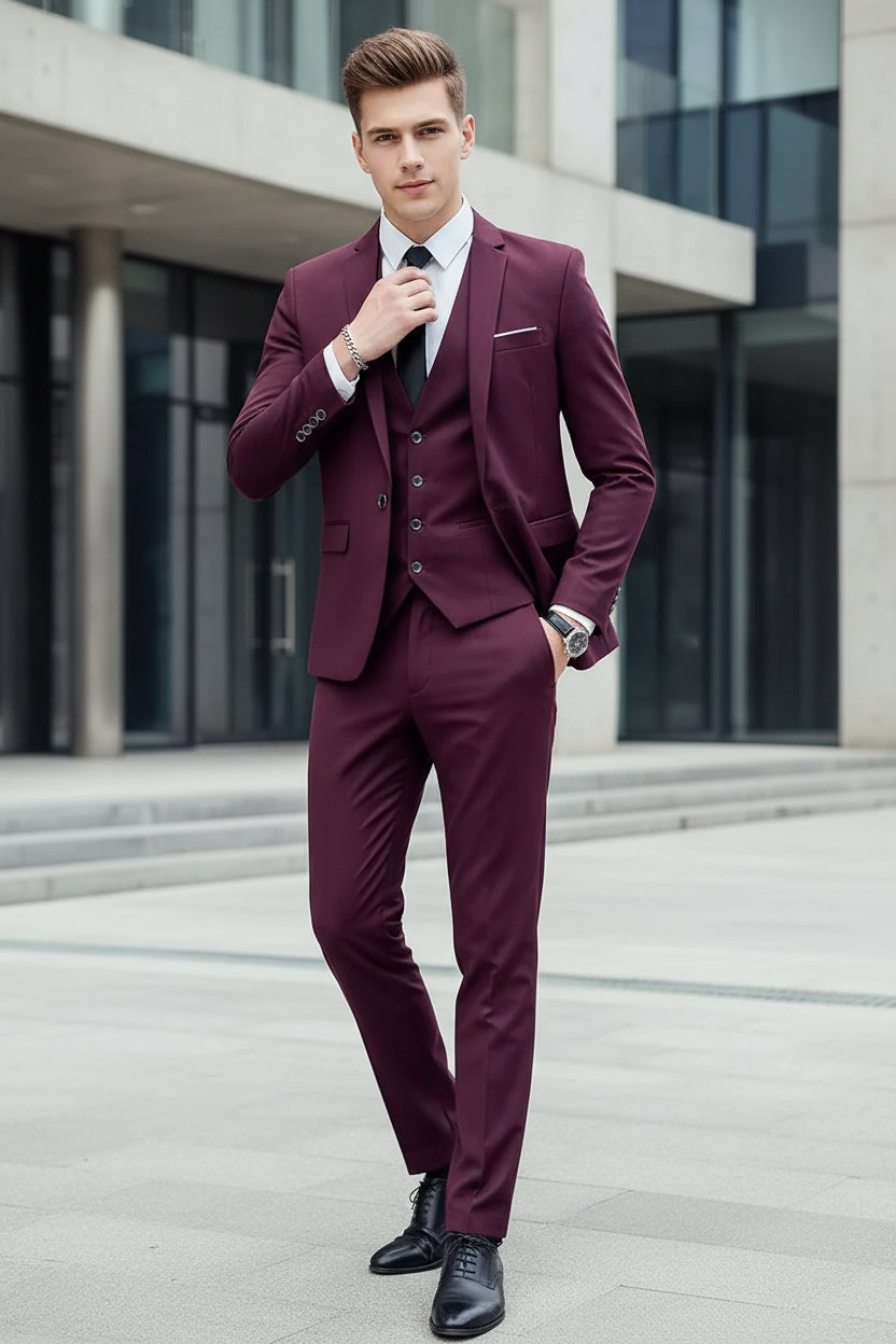 Man wearing a maroon suit with a white shirt and black tie against a concrete wall.