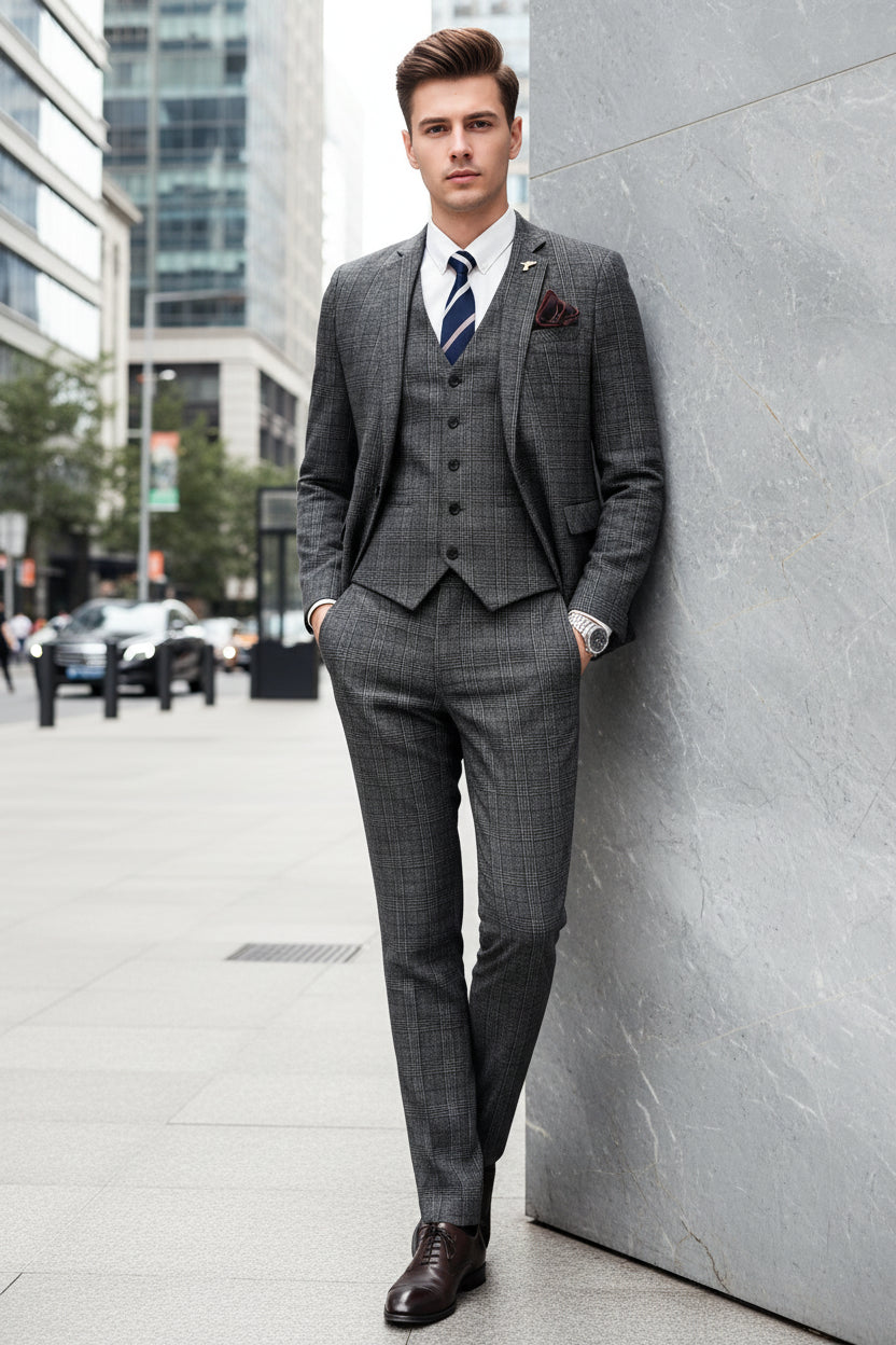 Man wearing a gray checkered suit with a white shirt and striped tie, holding a phone, standing against a marble wall.