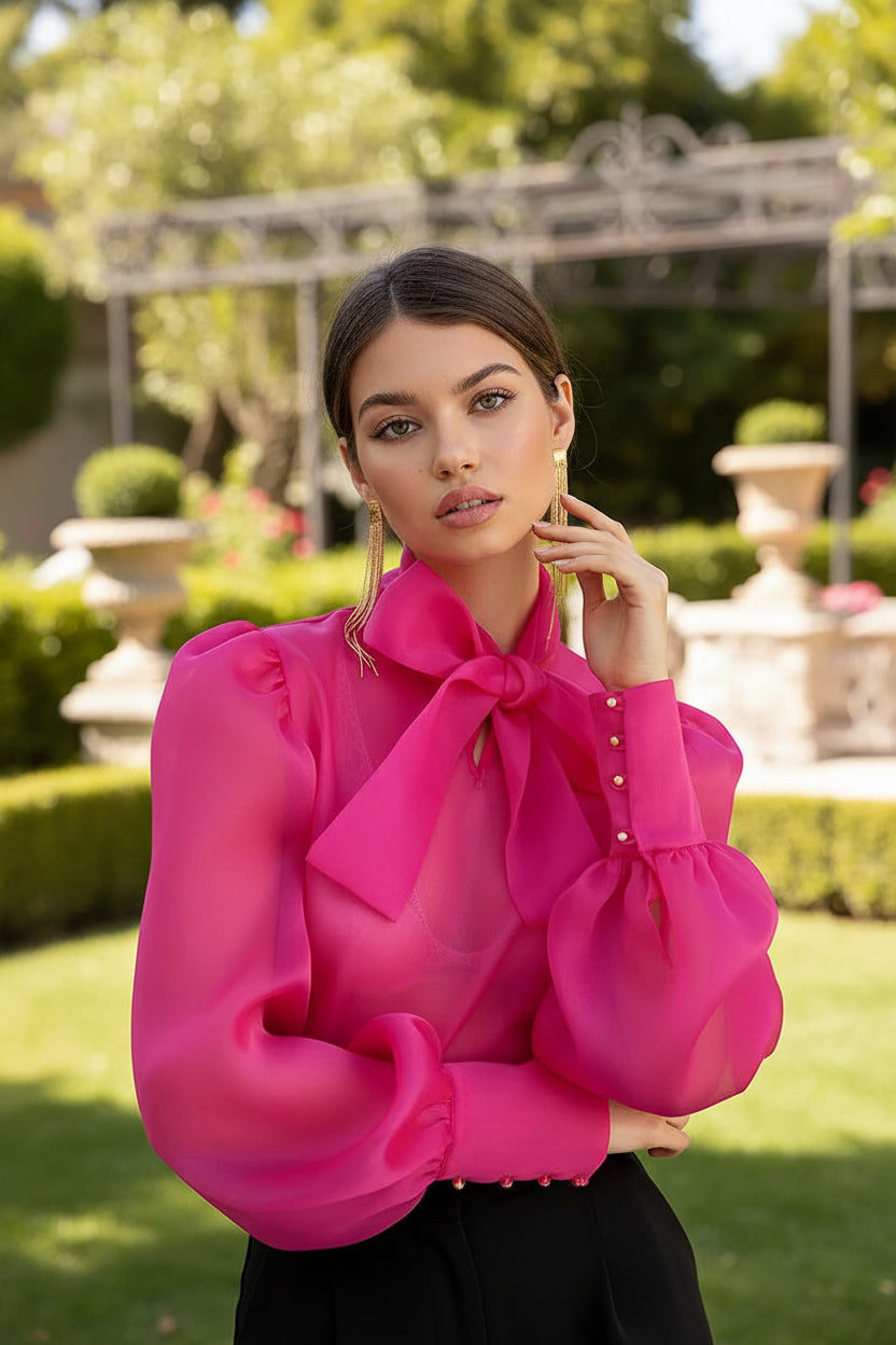Woman wearing a bright pink blouse with large bows on a plain background