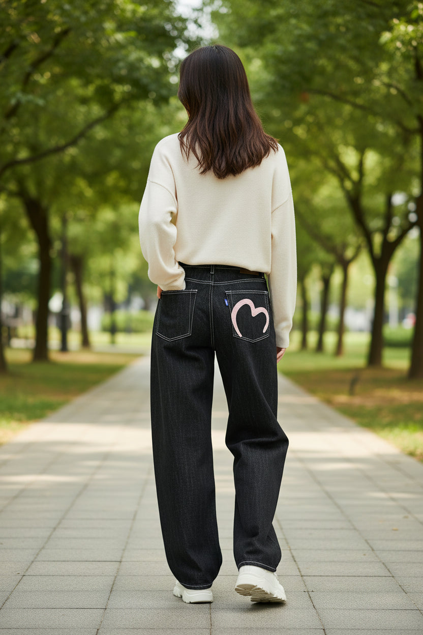 Black jeans with a pink heart design on the back pocket against a white background