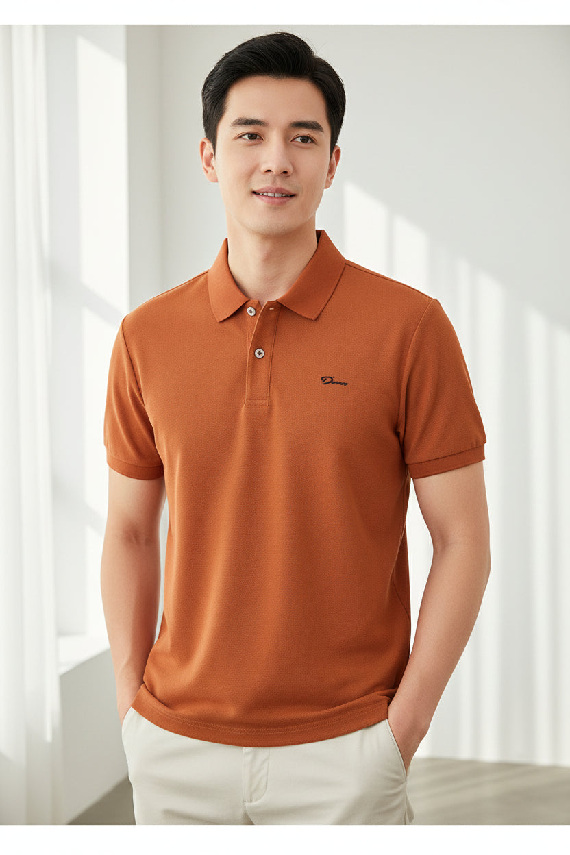 Orange polo shirt with a brand logo held by a hand, with more shirts in the background.