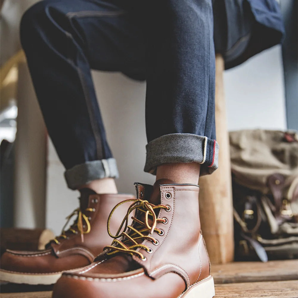 Brown leather boots with gold laces worn by a person sitting on a wooden chair.