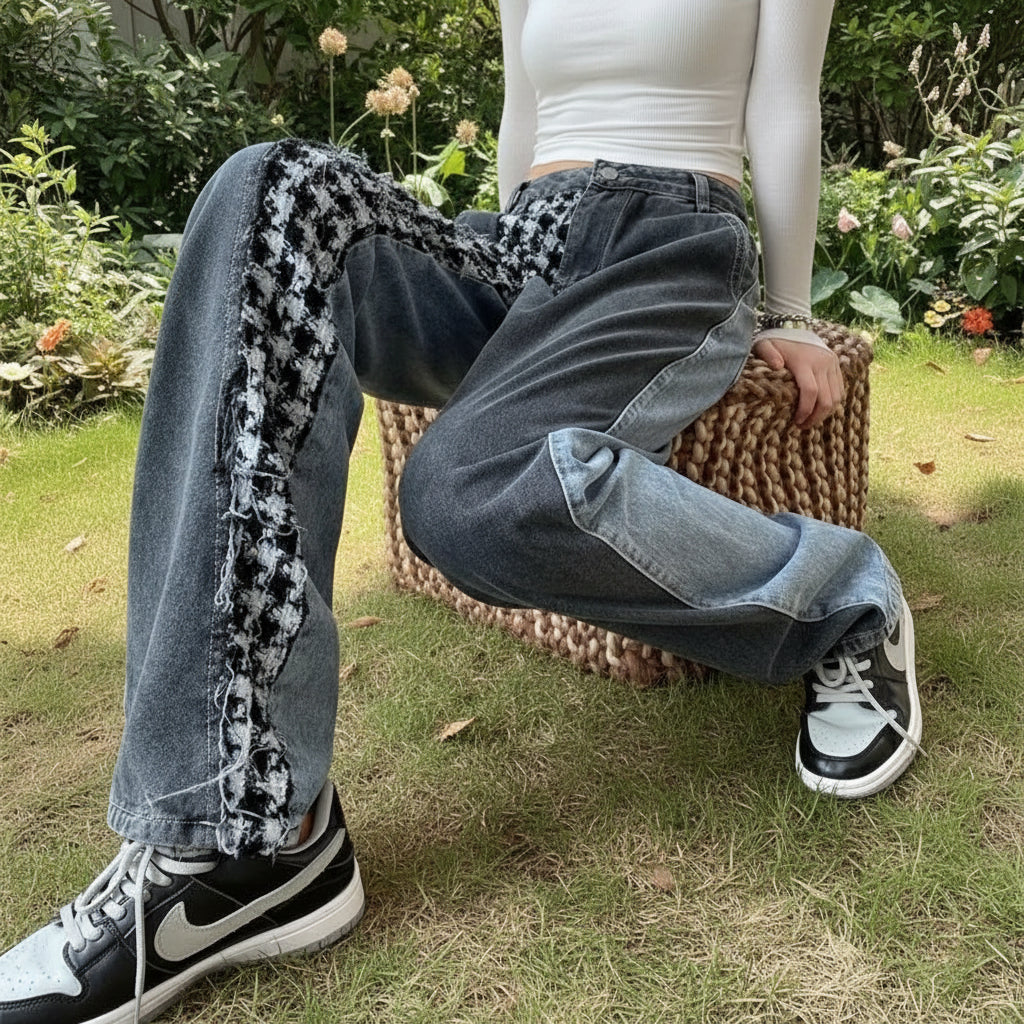 Person wearing blue jeans with patterned cuffs, white top, and black and white sneakers sitting on a woven stool.
