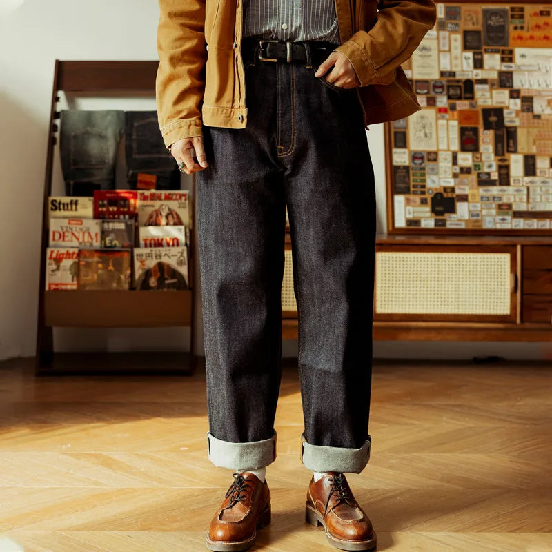 Person wearing a mustard jacket, dark jeans, and brown shoes in a room with a wooden floor and wall decorations.