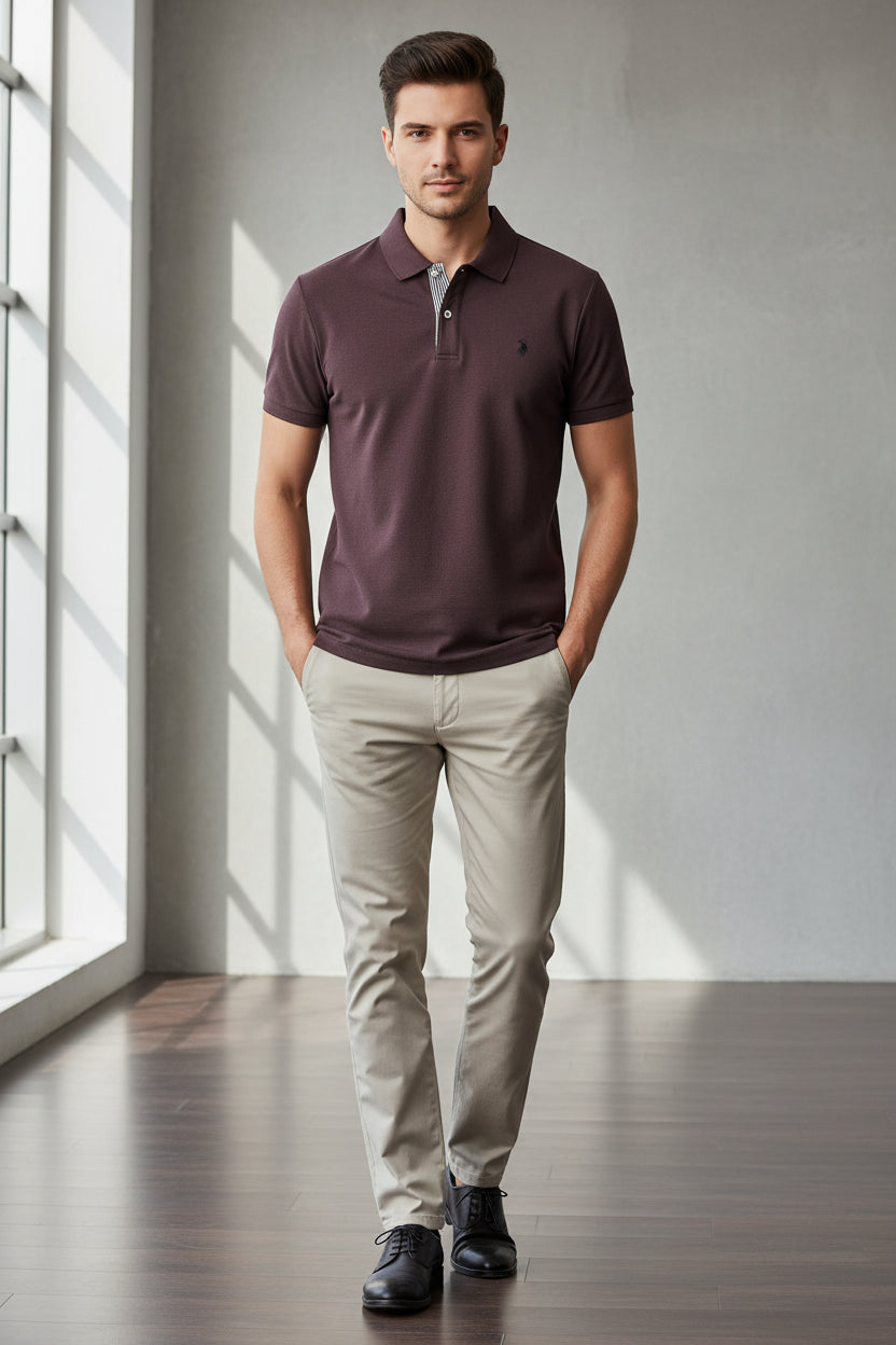 Purple polo shirt with a brand logo held by a hand, with other shirts in the background.