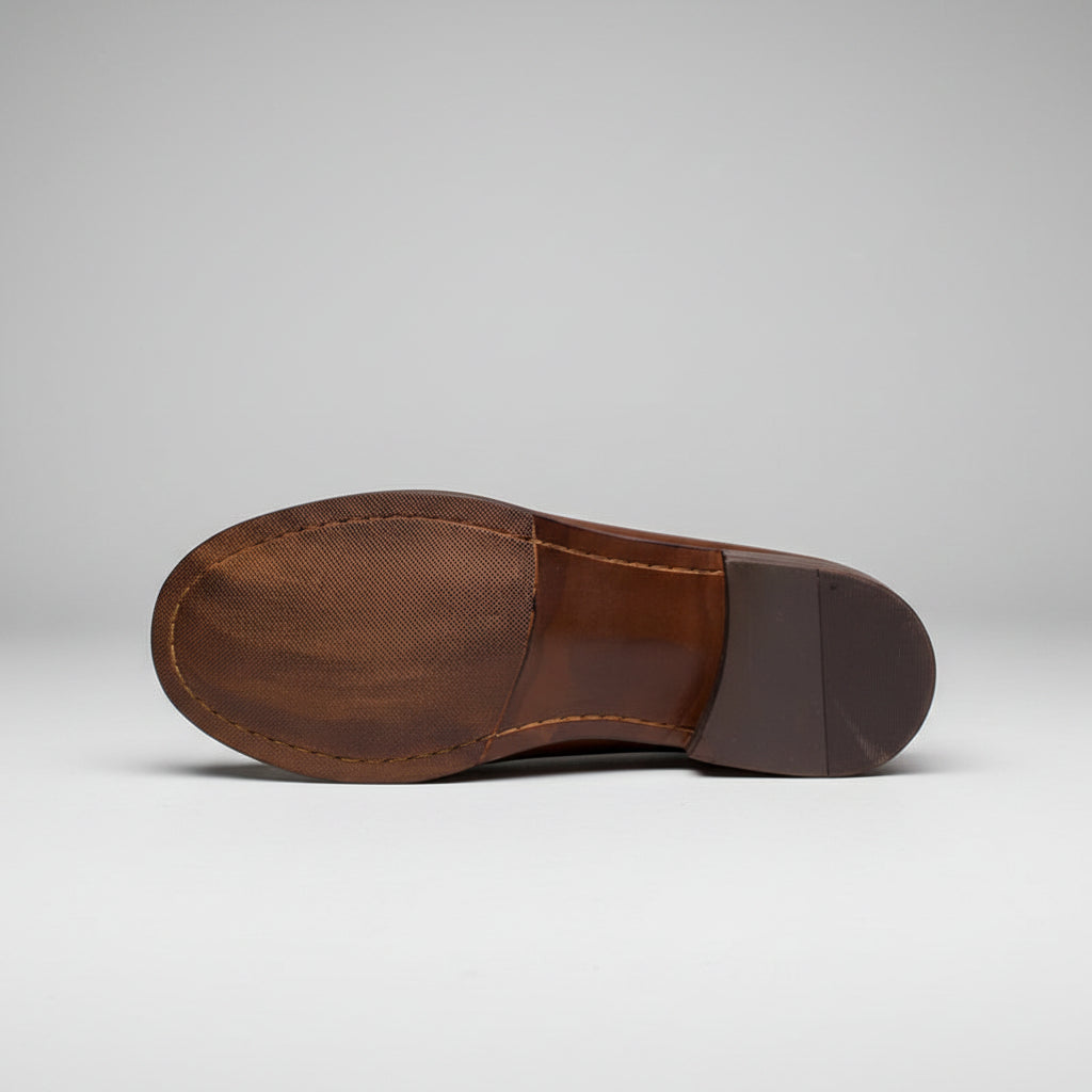 Close-up of a brown leather shoe sole on a wooden surface with a wooden chest in the background.
