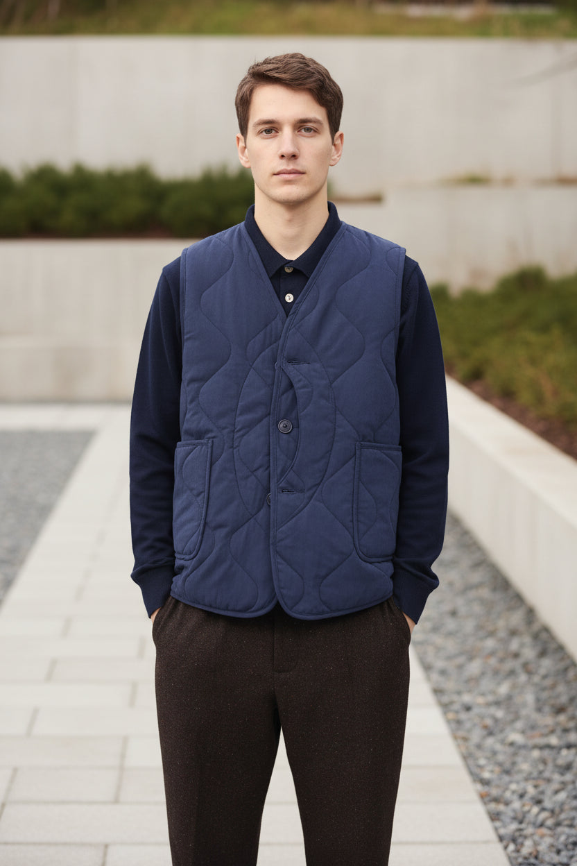 Person wearing a blue quilted vest over a dark shirt on a green background