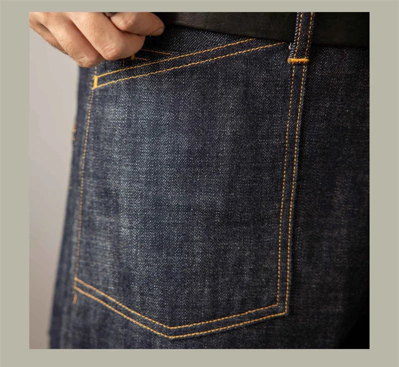 Close-up of a person wearing dark blue jeans with yellow stitching on a neutral background