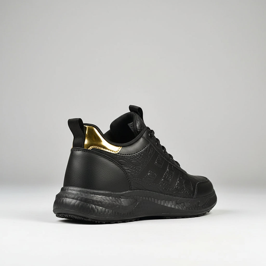 Black slip-on shoes with gold accents on a wooden floor.