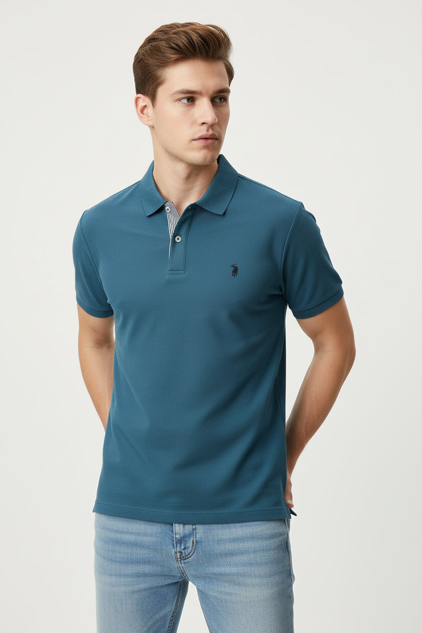 Blue polo shirt with a red logo held by a hand, with other shirts on hangers in the background.