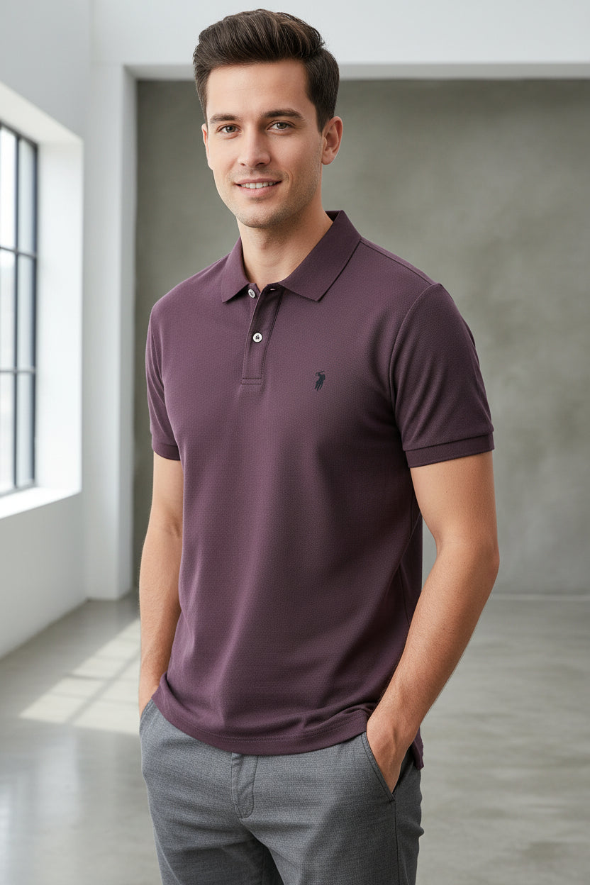 Purple polo shirt with a brand logo held by a hand, with other shirts in the background.