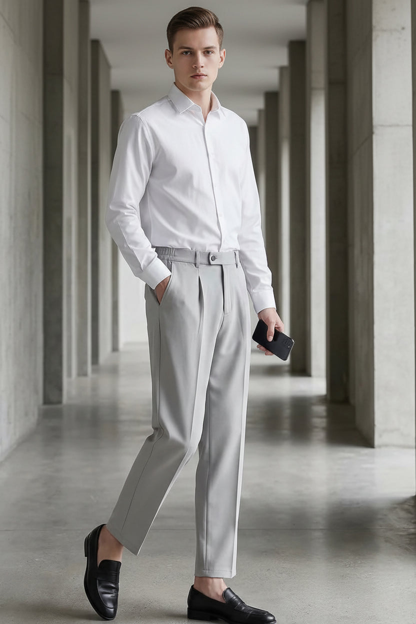 Person wearing light gray pants and a white shirt in a concrete hallway.