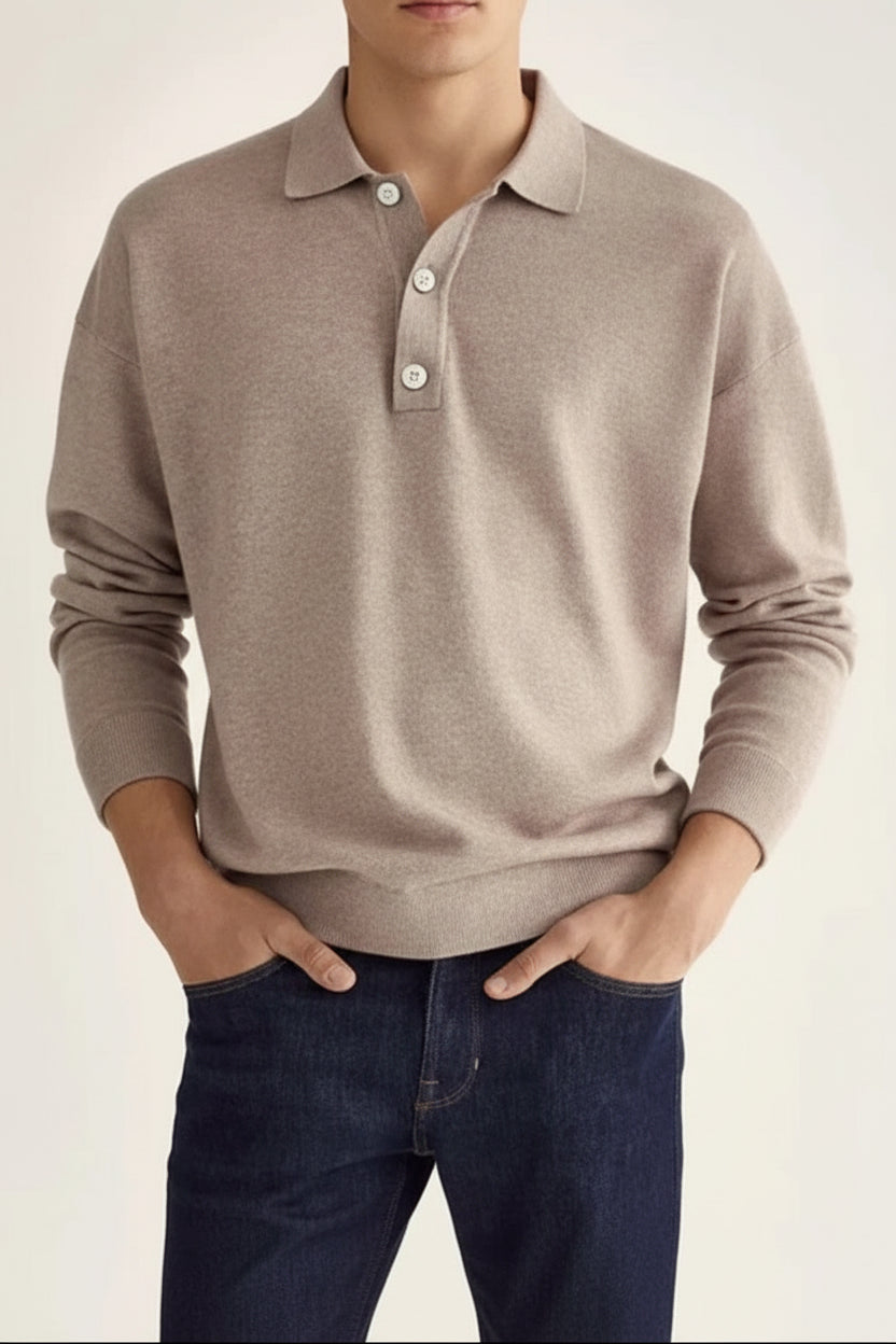Man wearing a beige long-sleeve polo shirt and dark jeans on a plain background