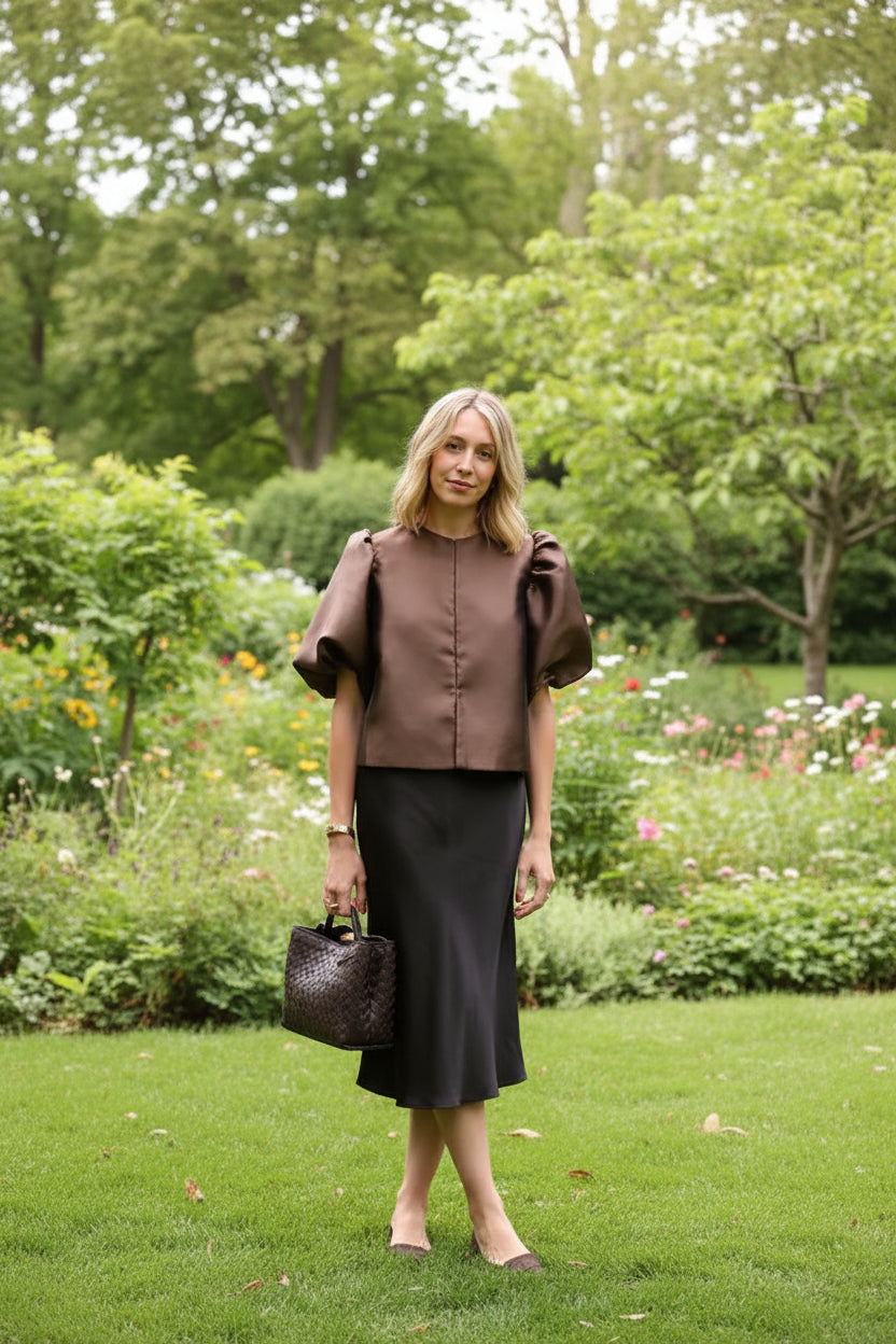 Woman in a brown top and black skirt holding a black handbag at night.