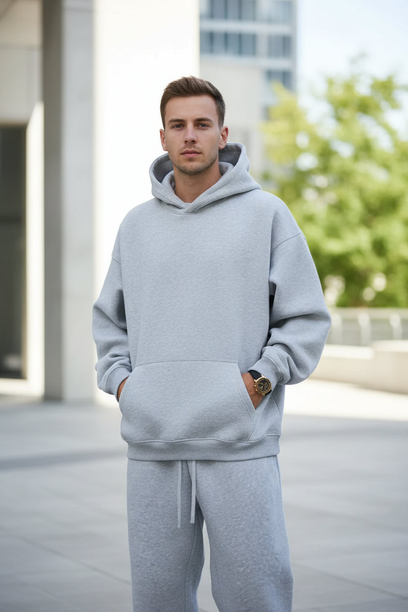 Person wearing a gray hoodie and pants with headphones on a white background