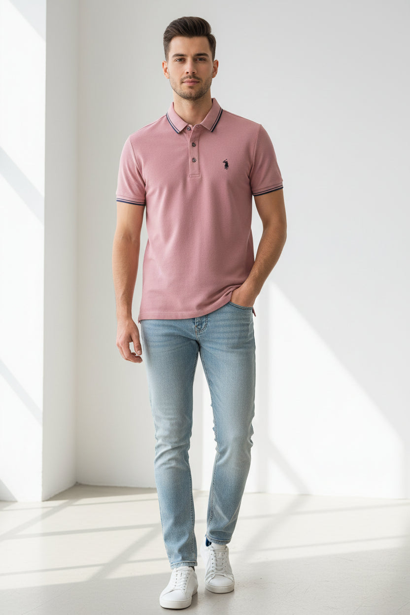 Pink polo shirt with a brand logo held by a hand, with books and clothing in the background.