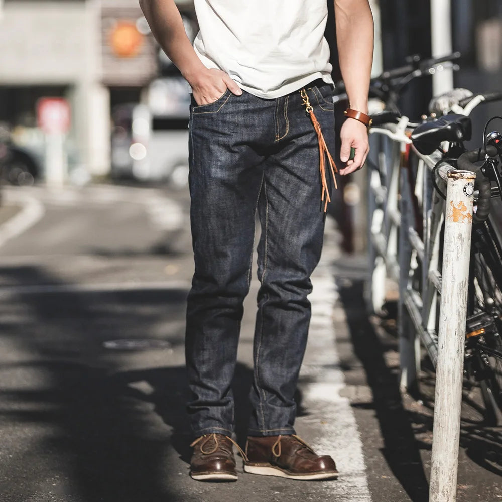 Person wearing dark jeans and brown shoes standing on a city street with bicycles in the background.