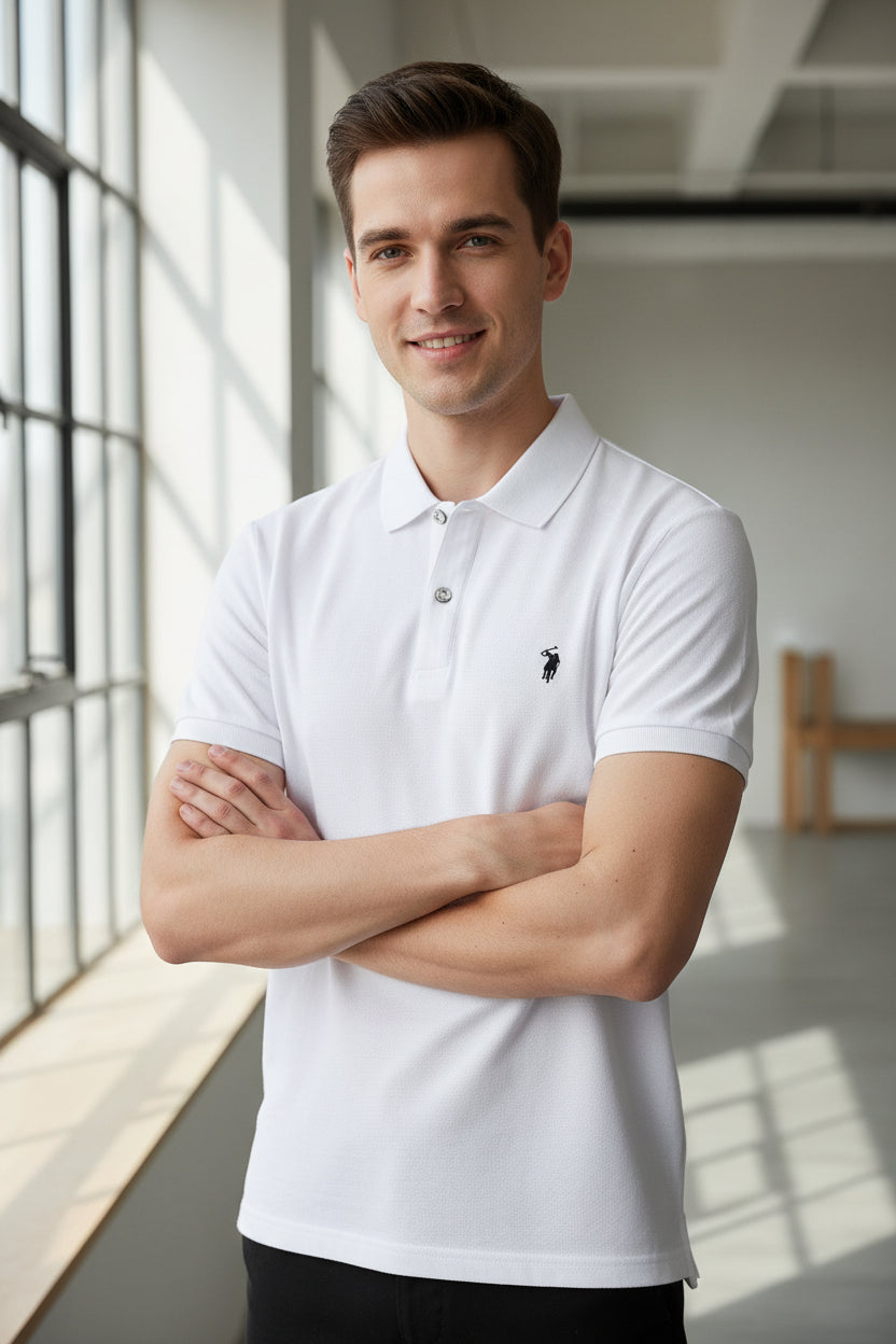 White polo shirt with a brand logo held by a hand, with other shirts in the background.