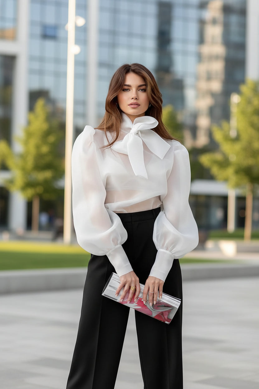 Woman wearing a white blouse with a bow tie and black pants against a gray background