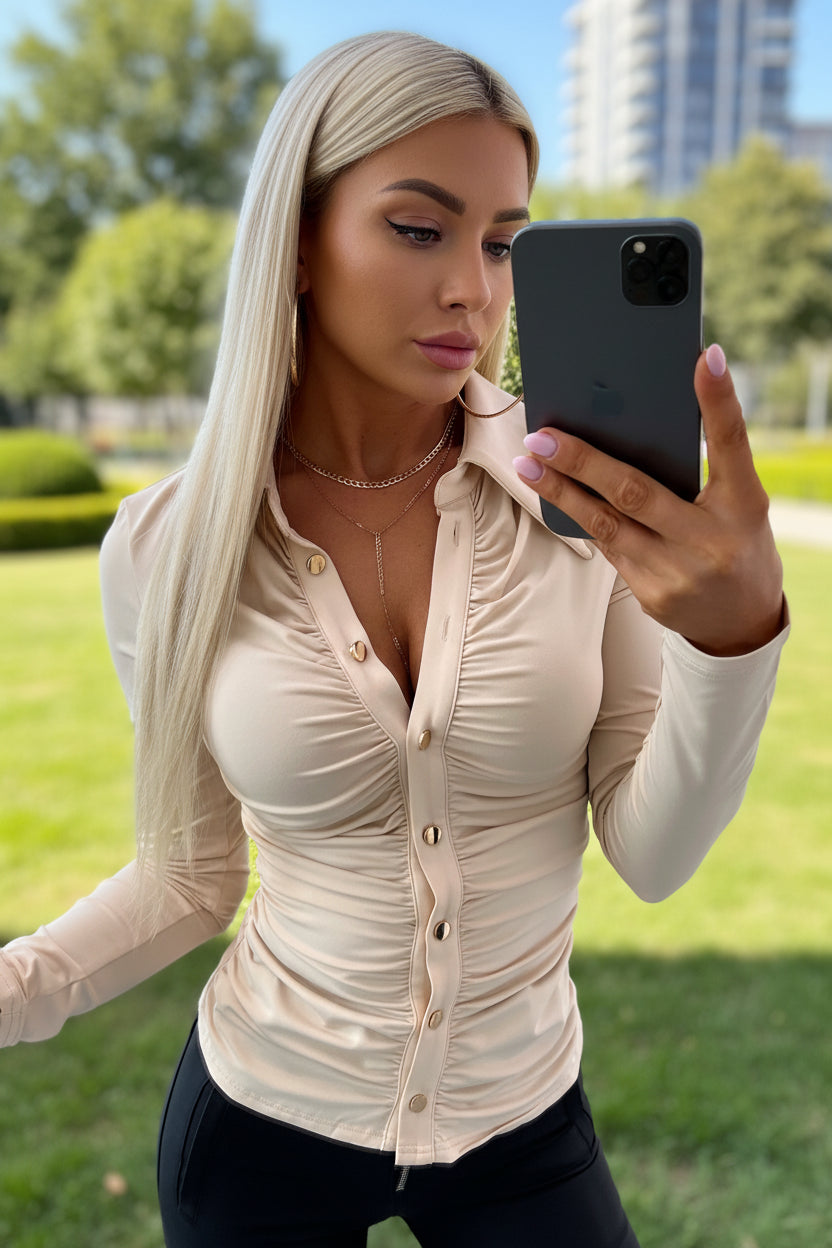Person wearing a beige button-up shirt with long sleeves, taking a mirror selfie.