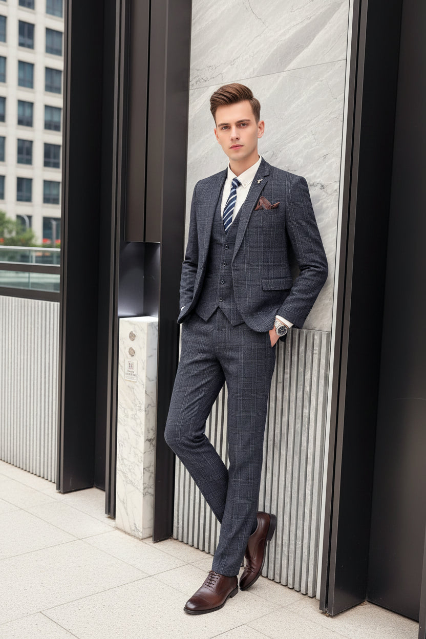 Person wearing a gray checkered suit with a striped tie, standing against a marble wall.