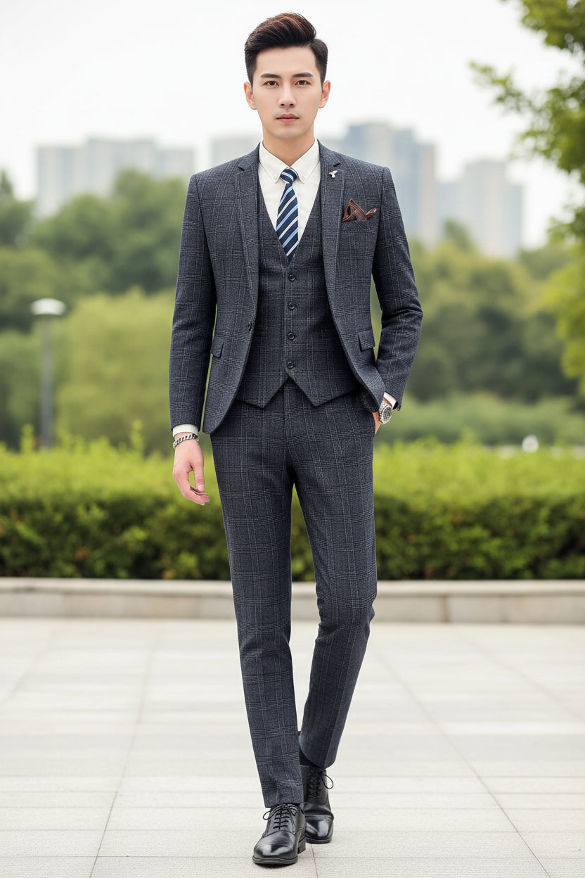 Person wearing a gray checkered suit with a striped tie, standing against a marble wall.