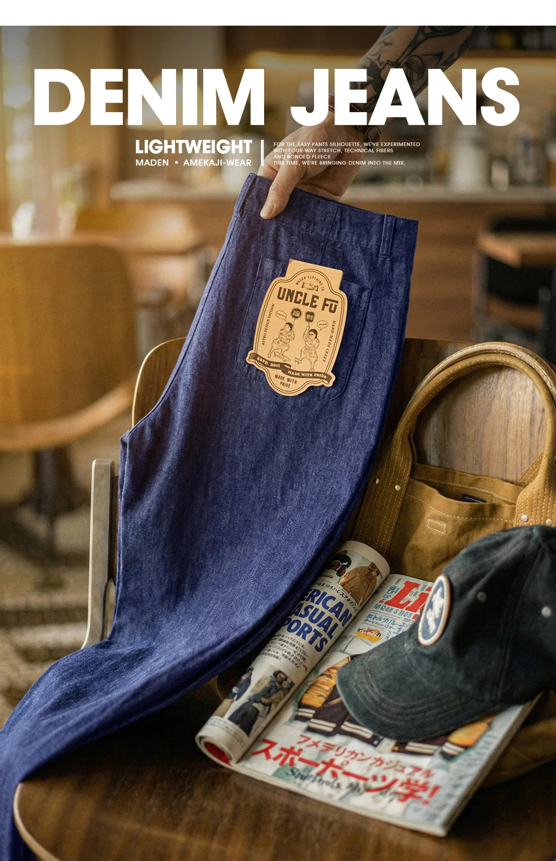 Blue denim jeans with a brand label held above a wooden table with a cap and magazine.