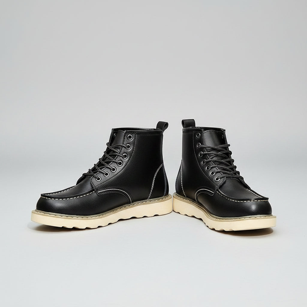 Black leather boots with white soles worn by a person on a rustic surface.
