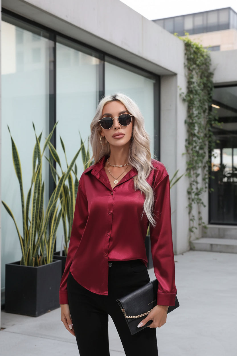 Woman wearing a red satin shirt and sunglasses, holding a black clutch against a white background