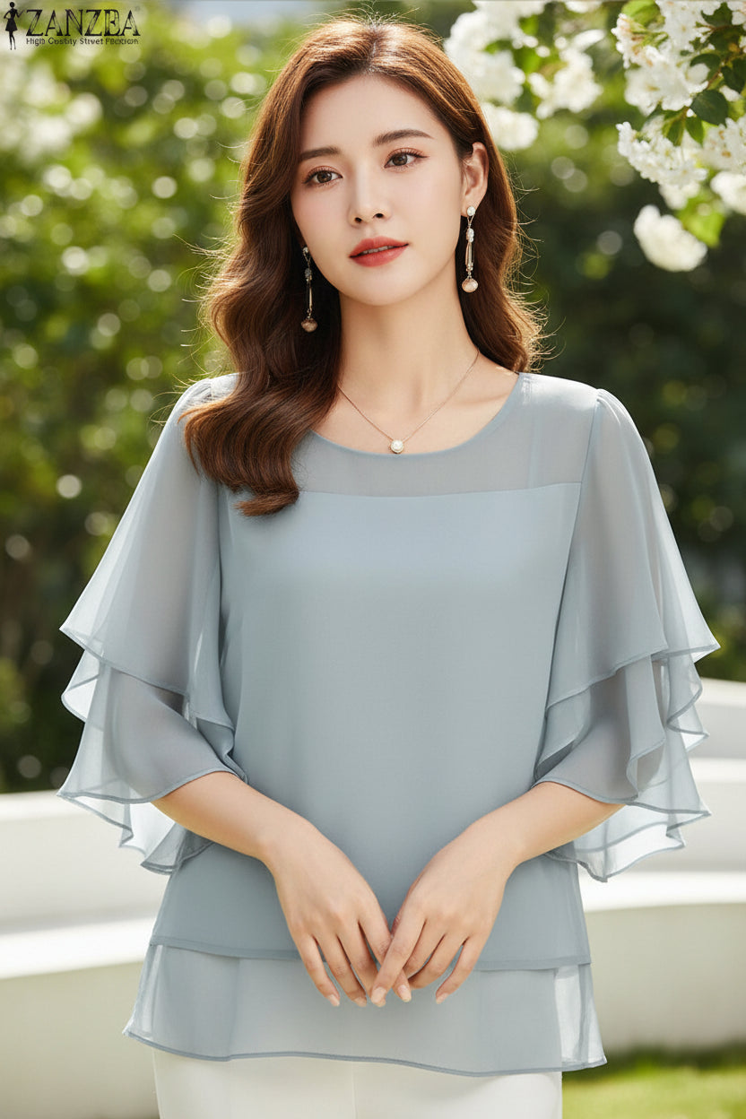 Woman wearing a light blue blouse with ruffled sleeves on a plain background