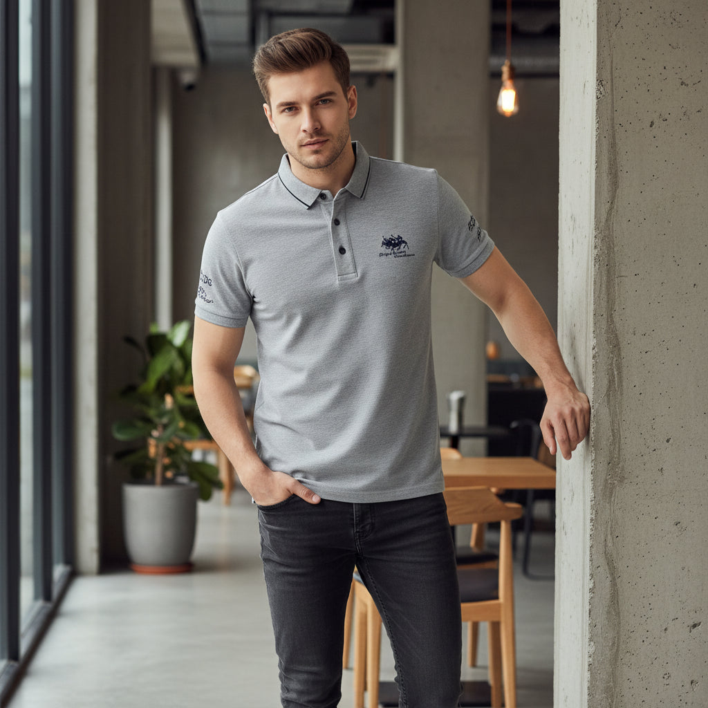 Folded gray polo shirt with brand logo on a dark surface, accompanied by a watch.