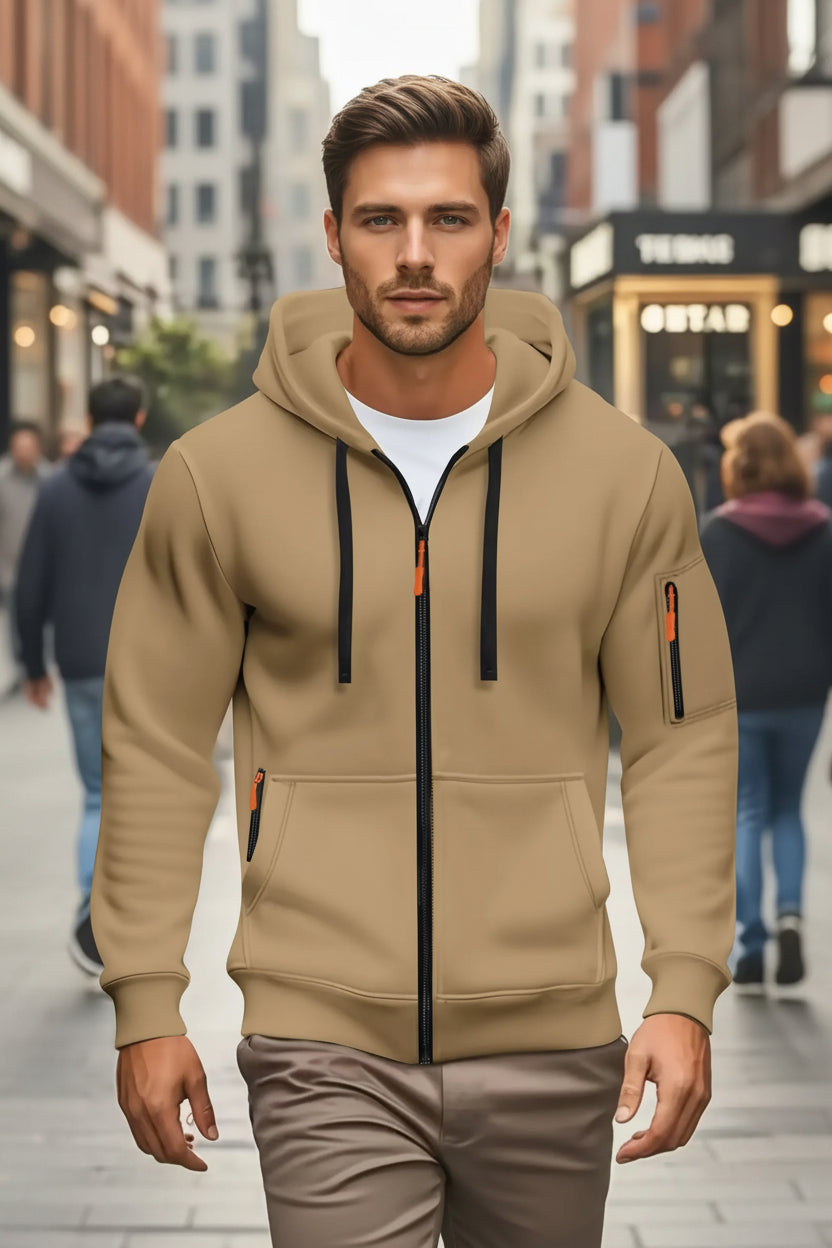 Man wearing a beige hoodie with black zipper and orange accents on a blurred street background