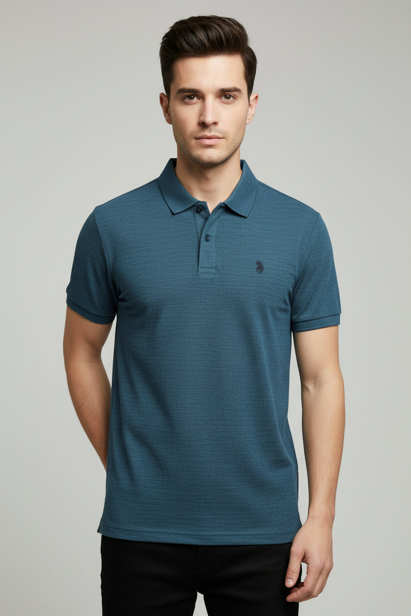 Hand holding a blue textured polo shirt with other shirts on a rack in the background.