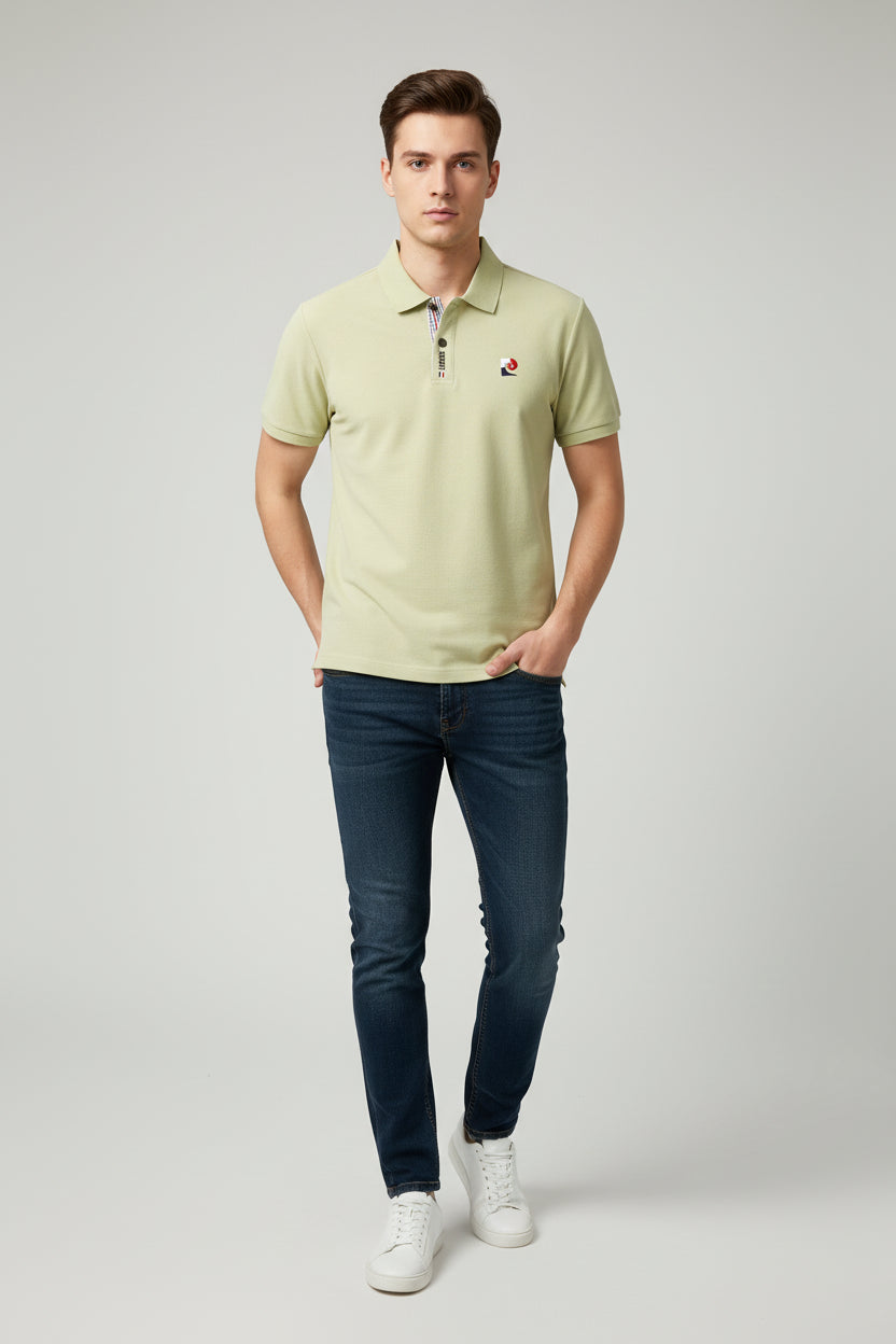 Light green polo shirt with brand logo held by a hand, hanging on a rack with other shirts.