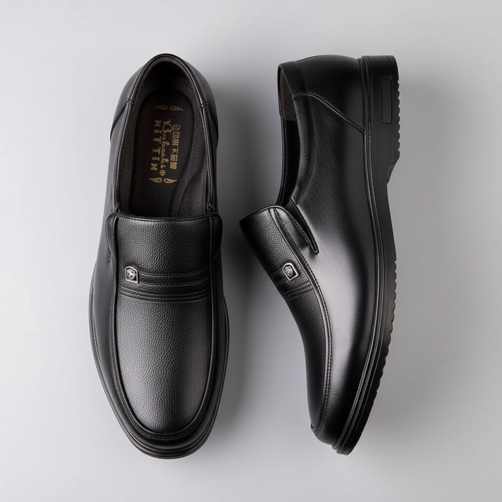 Pair of black leather shoes on a wooden surface with a pen and watch in the background.