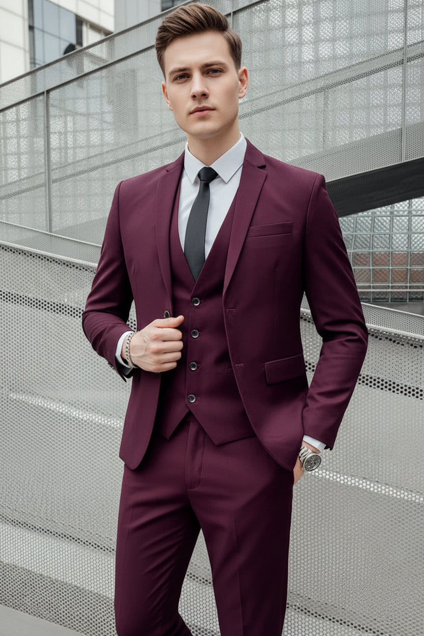 Man wearing a burgundy suit with a white shirt and black tie against a metallic background