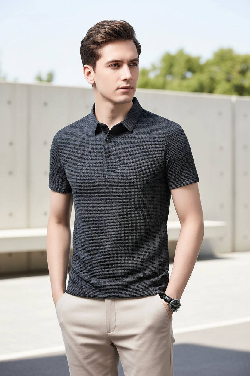Man wearing a dark patterned polo shirt against a gray background
