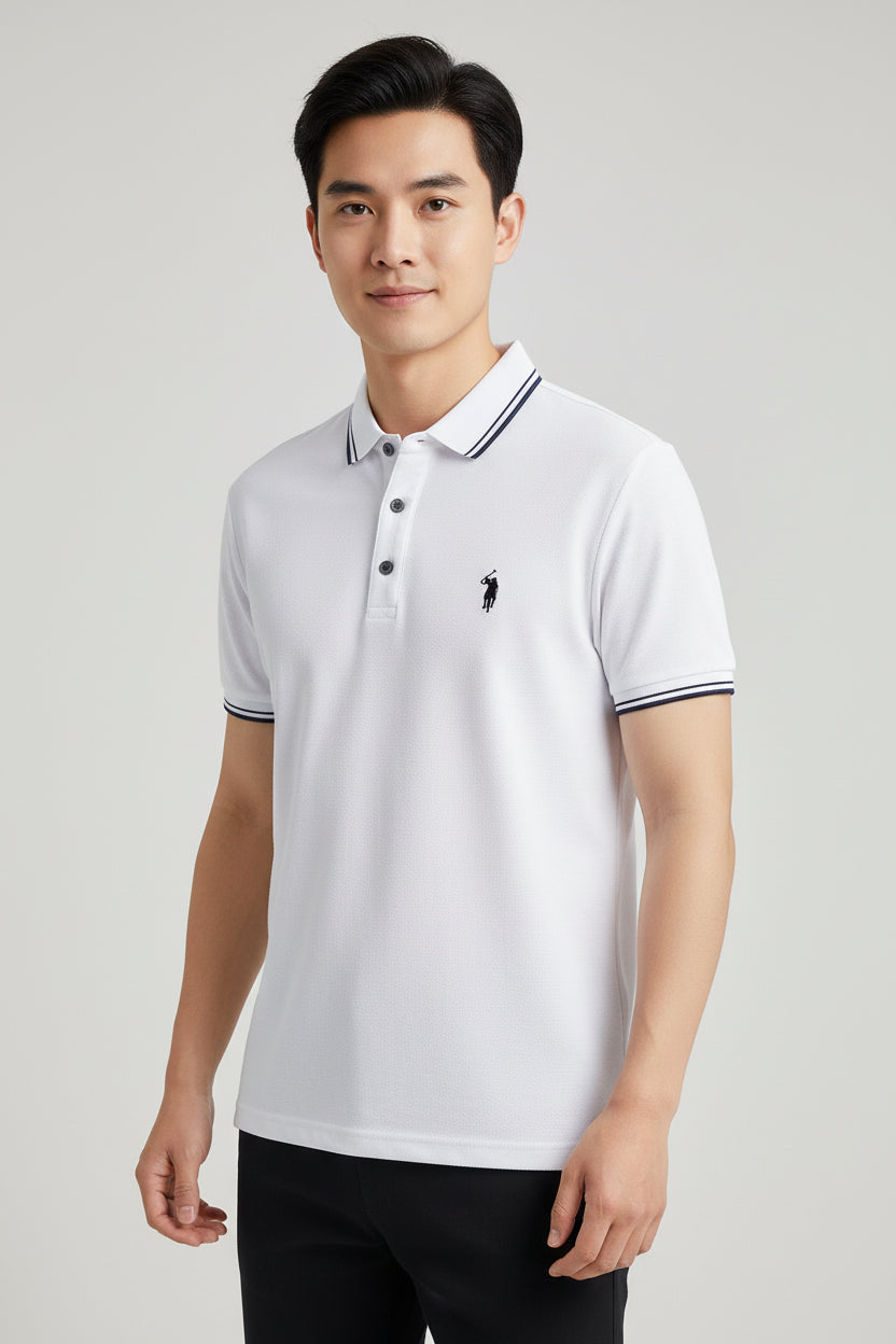 White polo shirt with black logo held by a hand, with a blurred background of books and clothing.