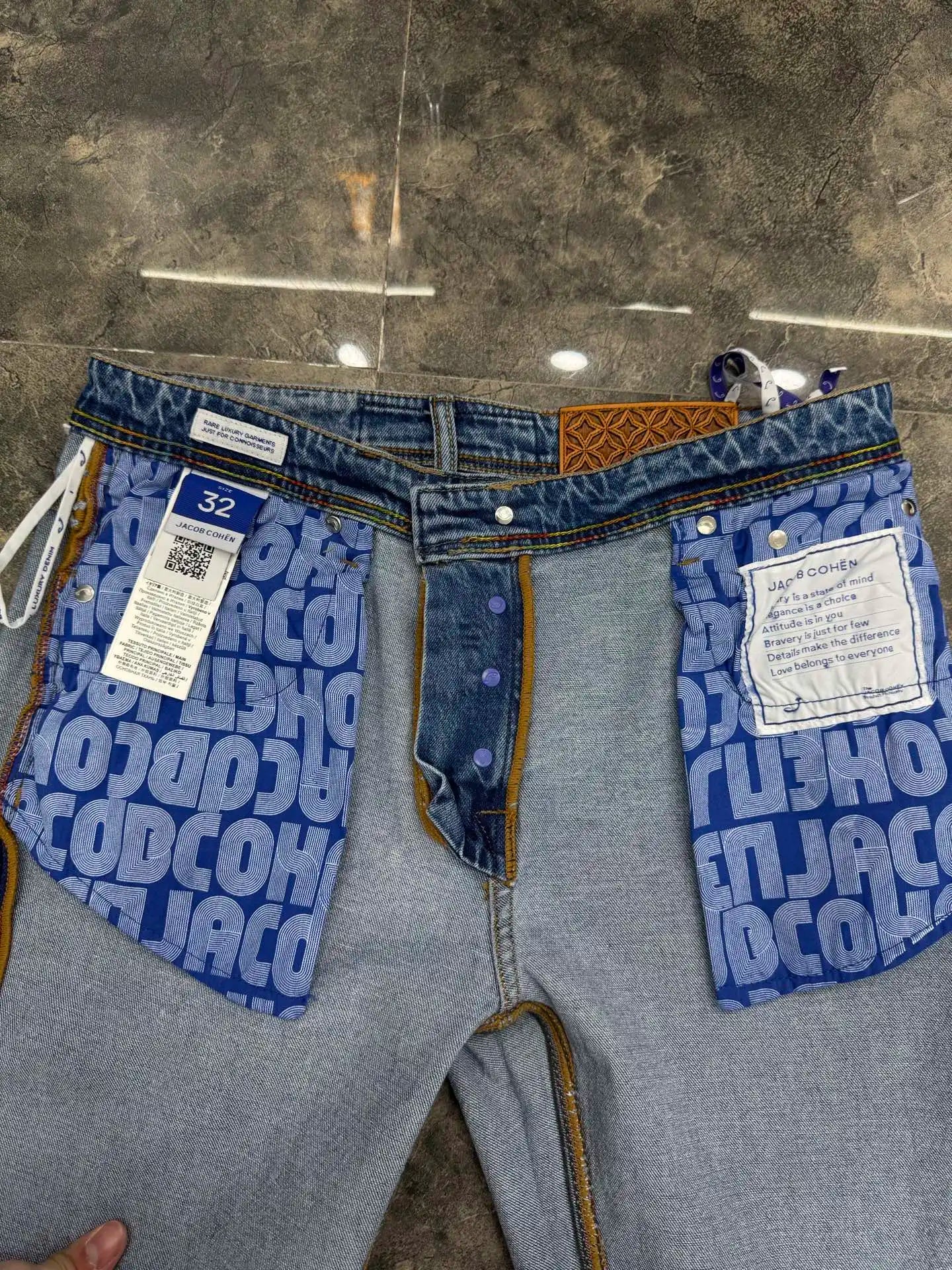 Gray jeans with blue patterned back pockets on a concrete floor.