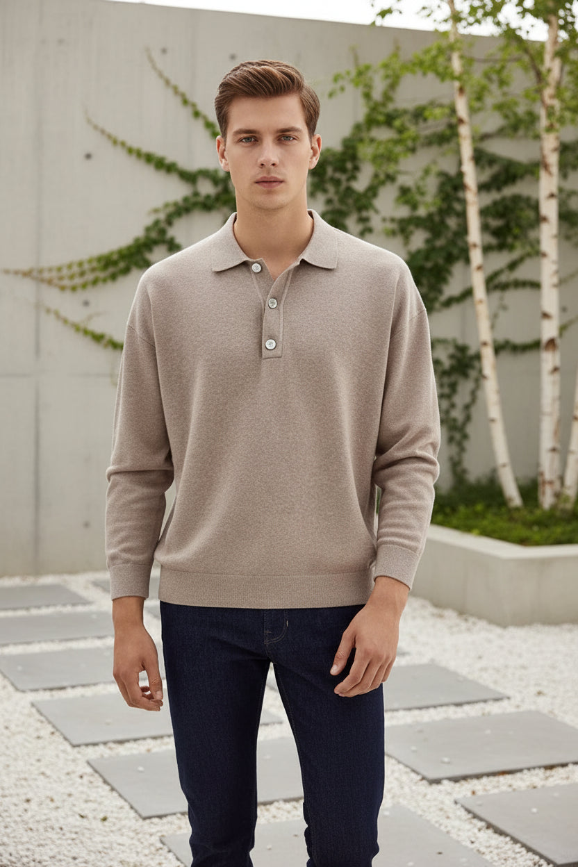 Man wearing a beige long-sleeve polo shirt and dark jeans on a plain background