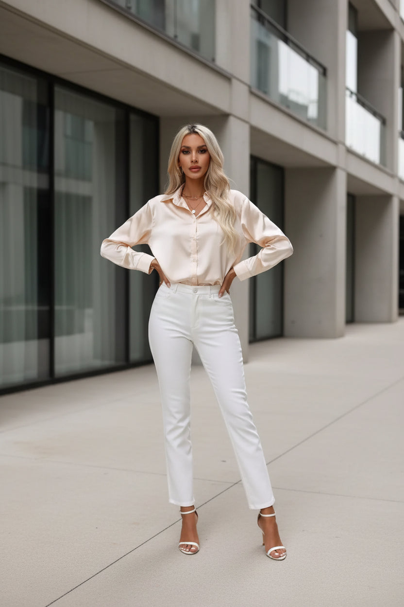 Woman wearing a beige blouse and white pants sitting on a chair in a bright room.