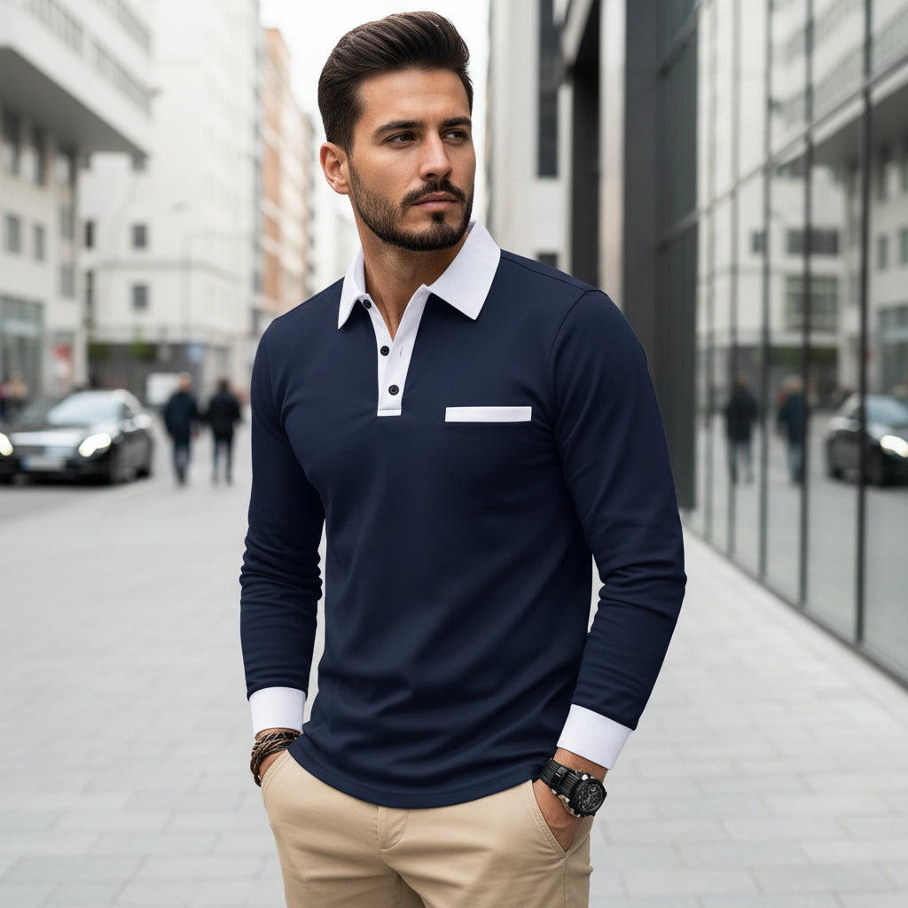 Man wearing a navy long-sleeve polo shirt with white collar and cuffs, standing against a reflective surface.