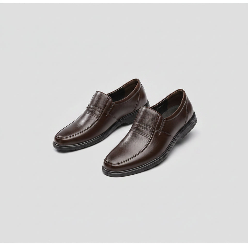 Brown leather shoes worn with gray pants on a carpeted floor.