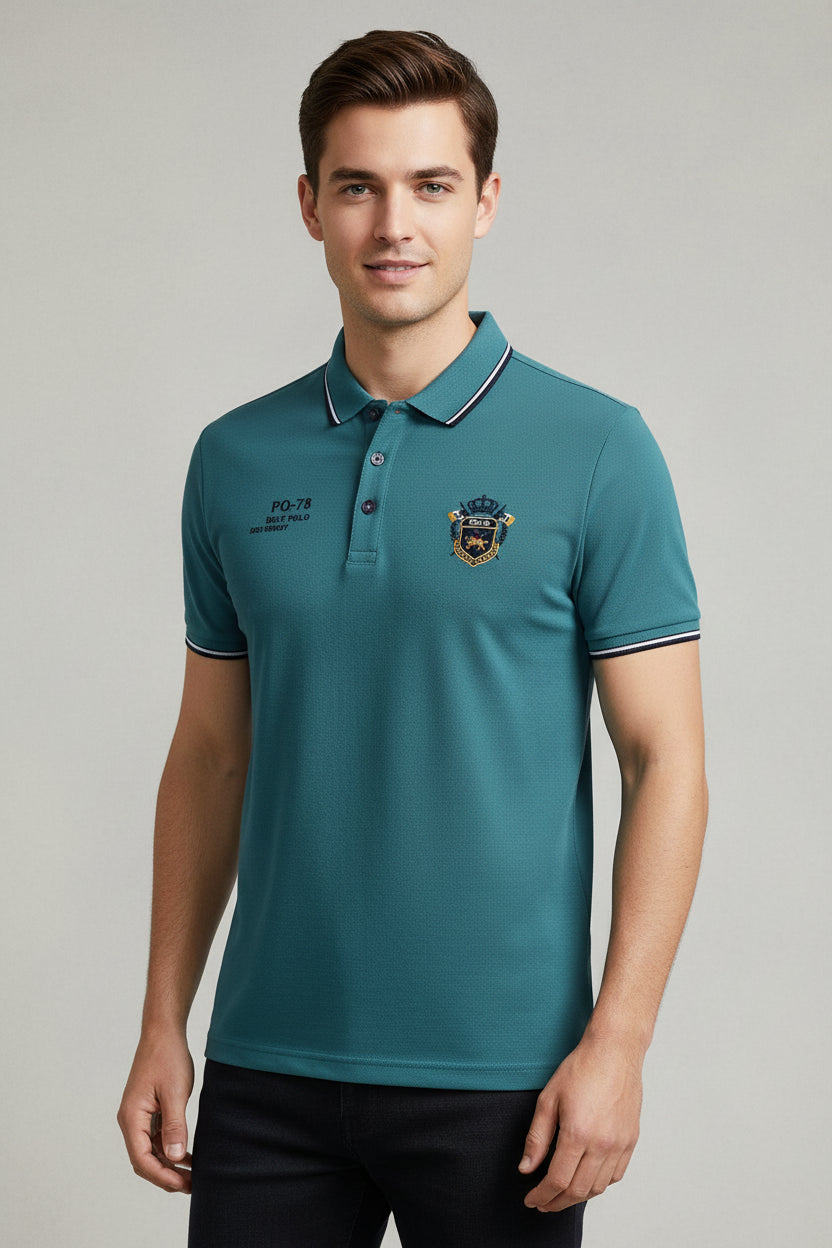 Teal polo shirt with a logo and a watch on a gray surface