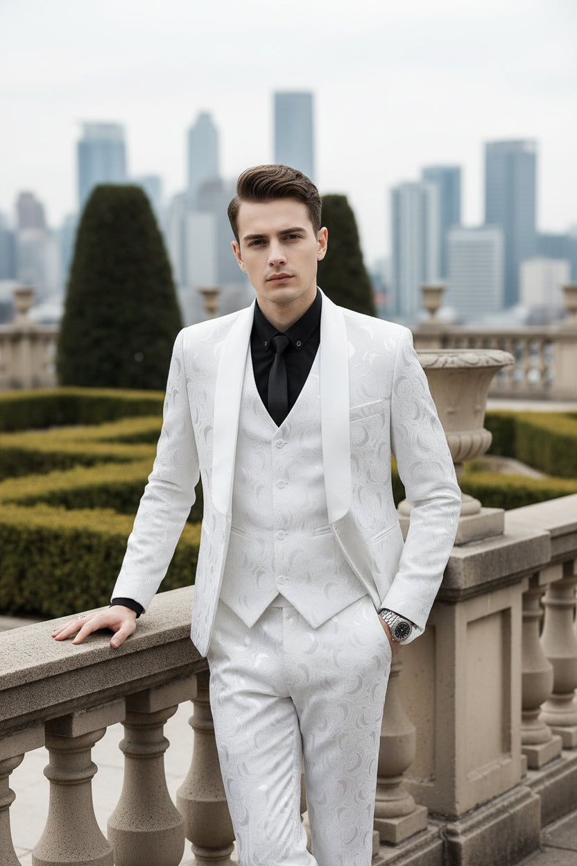 Man wearing a white patterned suit with a black shirt and tie indoors.