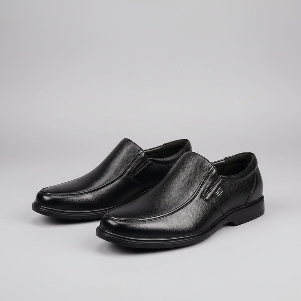 Black leather shoes worn with black socks on a gray floor.